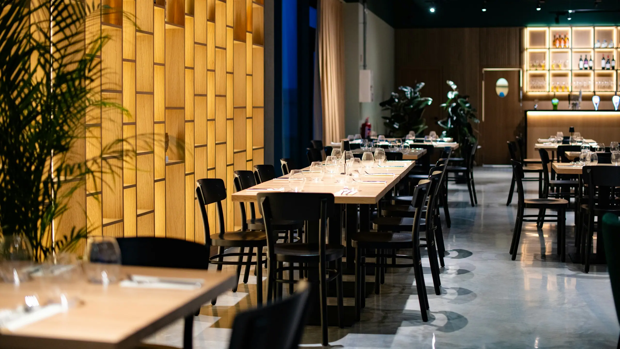 Restaurant mit Holzwand, langen Tischen und warmem Licht
