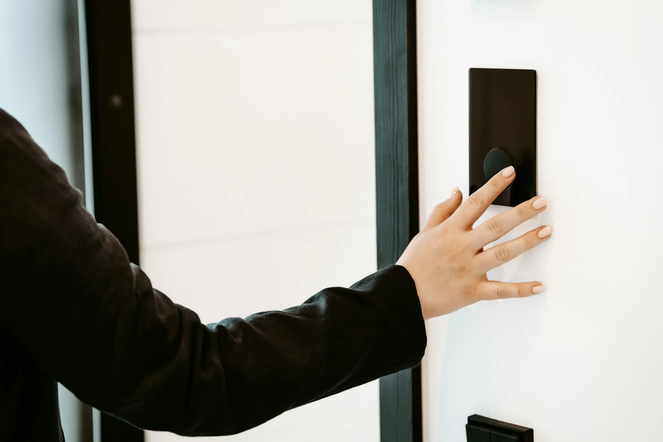 Hand bedient ein schlichtes, schwarzes Bedienfeld an einer hellen Wand